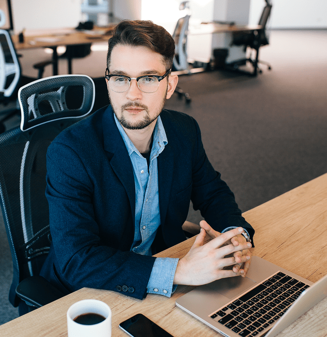 attractive-dark-haired-man-is-sitting-table-office-he-wears-blue-shirt-with-black-jacket-he-is-looking-side-view-from 1